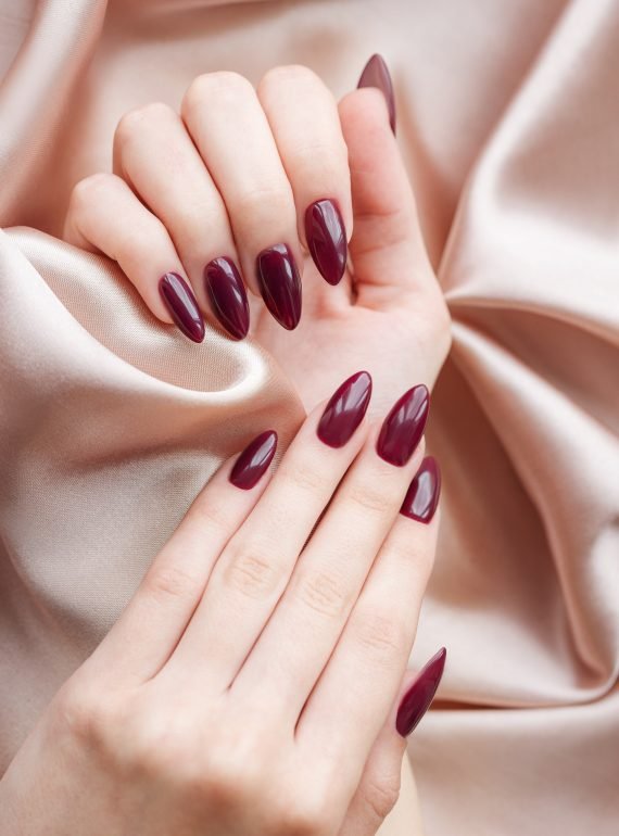 Beautiful hands of a young woman with dark red manicure on nails. Beige silk background